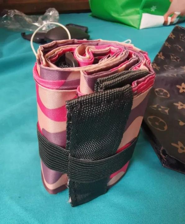 Compact foldable shopping bags set rolled up with black strap on a teal surface