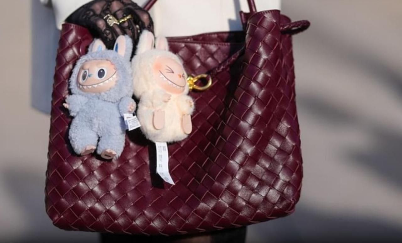 Two small Labubu dolls hanging from a maroon woven handbag in Labubu doll online India
