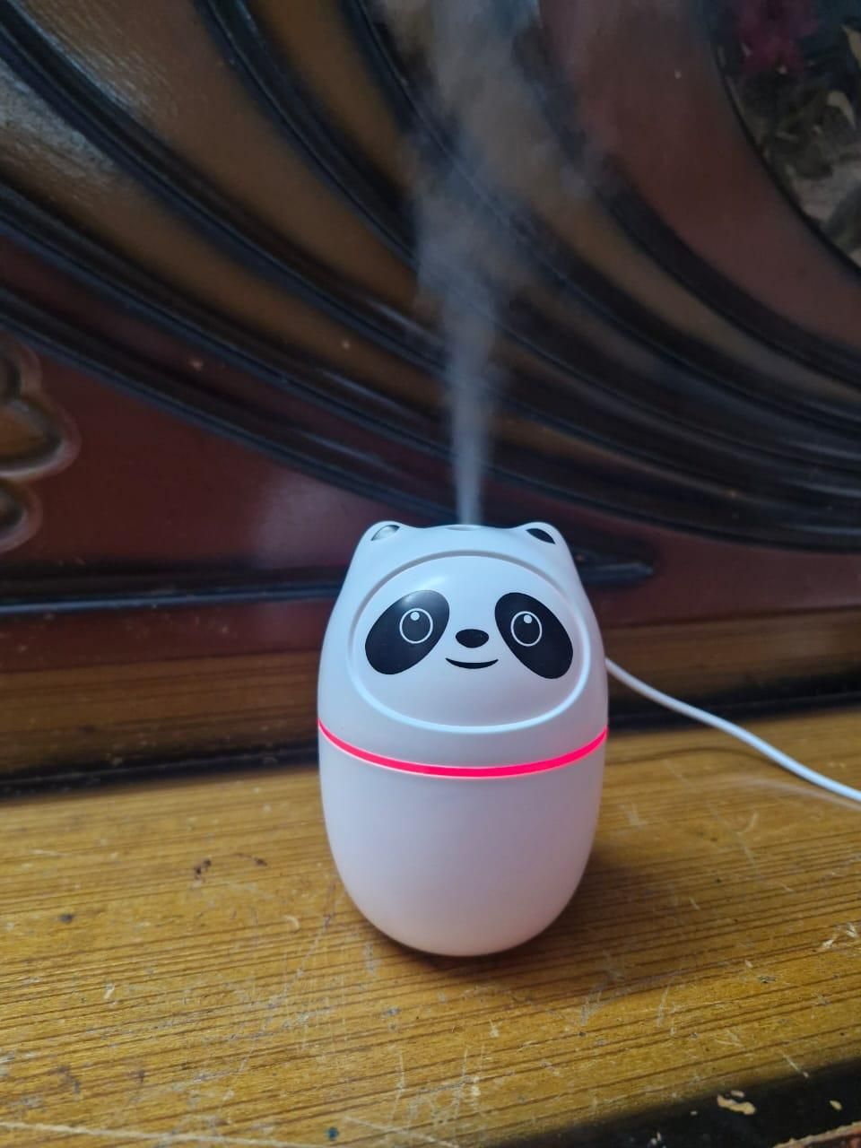 Panda-shaped mini cool mist humidifier for room emitting mist on wooden surface with cable