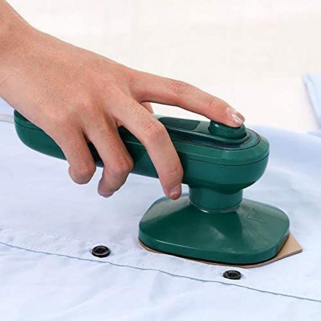 Hand using green portable clothes steamer to remove wrinkles from light blue shirt fabric