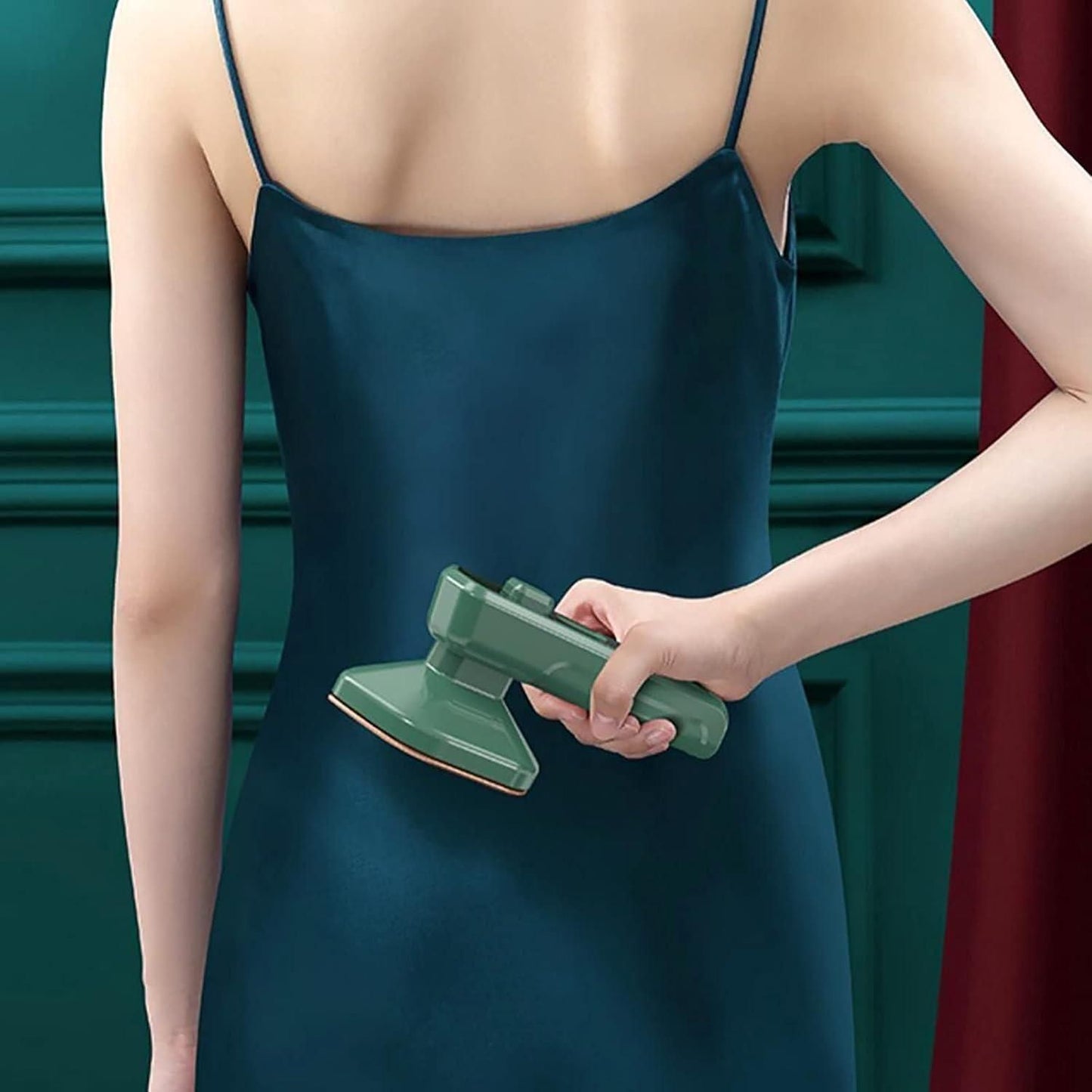 Person using a green portable clothes steamer on a dark blue satin dress from the back