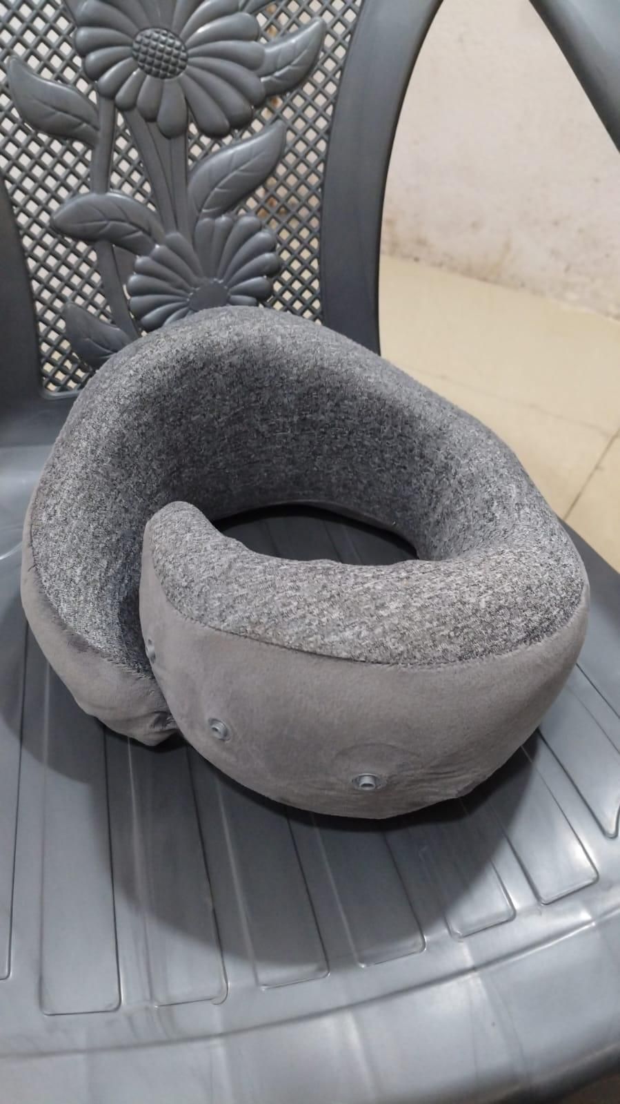 Gray portable neck pillow with carry bag resting on a dark plastic chair with floral design