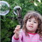 Child playing with 8 hole bubble gun toy for kids with batteries creating many bubbles outdoors