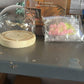 Decorative flower LED lamp with glass dome and wooden base beside packaging box and wrapped flower parts