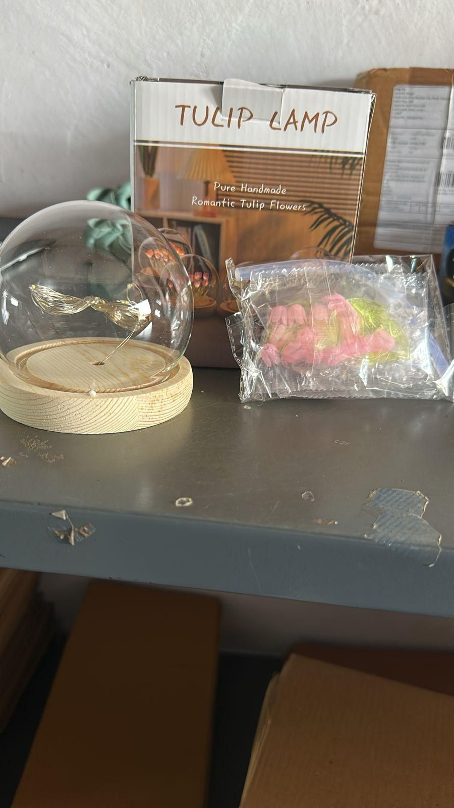 Decorative flower LED lamp with glass dome and wooden base beside packaging box and wrapped flower parts