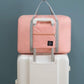 Pink carry on duffel bag for women with gray handles placed on top of white suitcase
