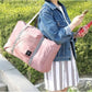 Pink carry on duffel bag for women with gray straps worn over shoulder by woman in denim jacket