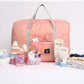 Pink carry on duffel bag for women with gray handles surrounded by baby bottles, lotion, pacifiers, and folded baby clothes