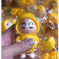 Hand holding a yellow Shinchan cartoon keychain India figure with packaged keychains in the background