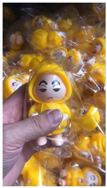 Hand holding a yellow Shinchan cartoon keychain India figure with packaged keychains in the background
