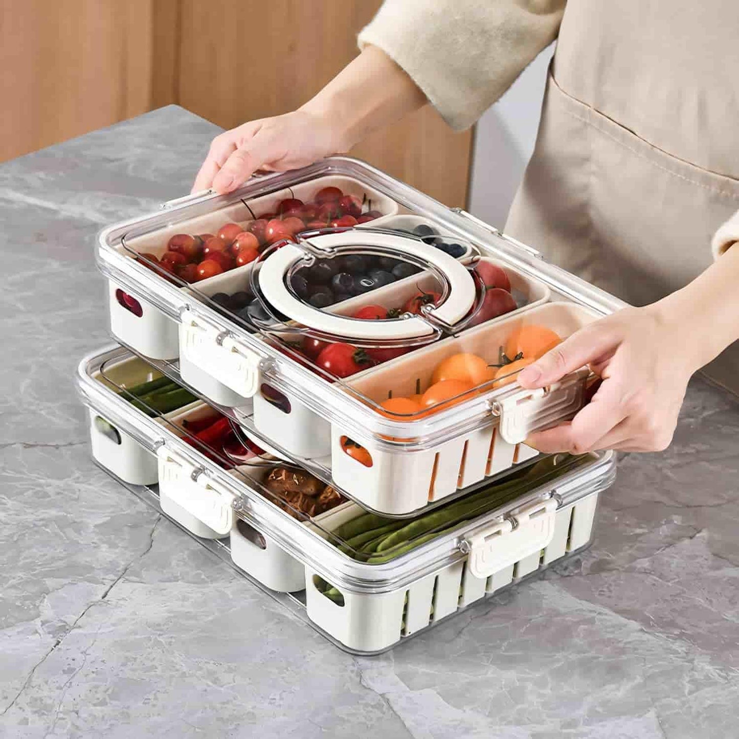 Clear fridge storage container with compartments holding fruits and vegetables stacked on a kitchen counter