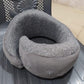 Gray portable neck pillow with carry bag resting on a dark plastic chair with floral design
